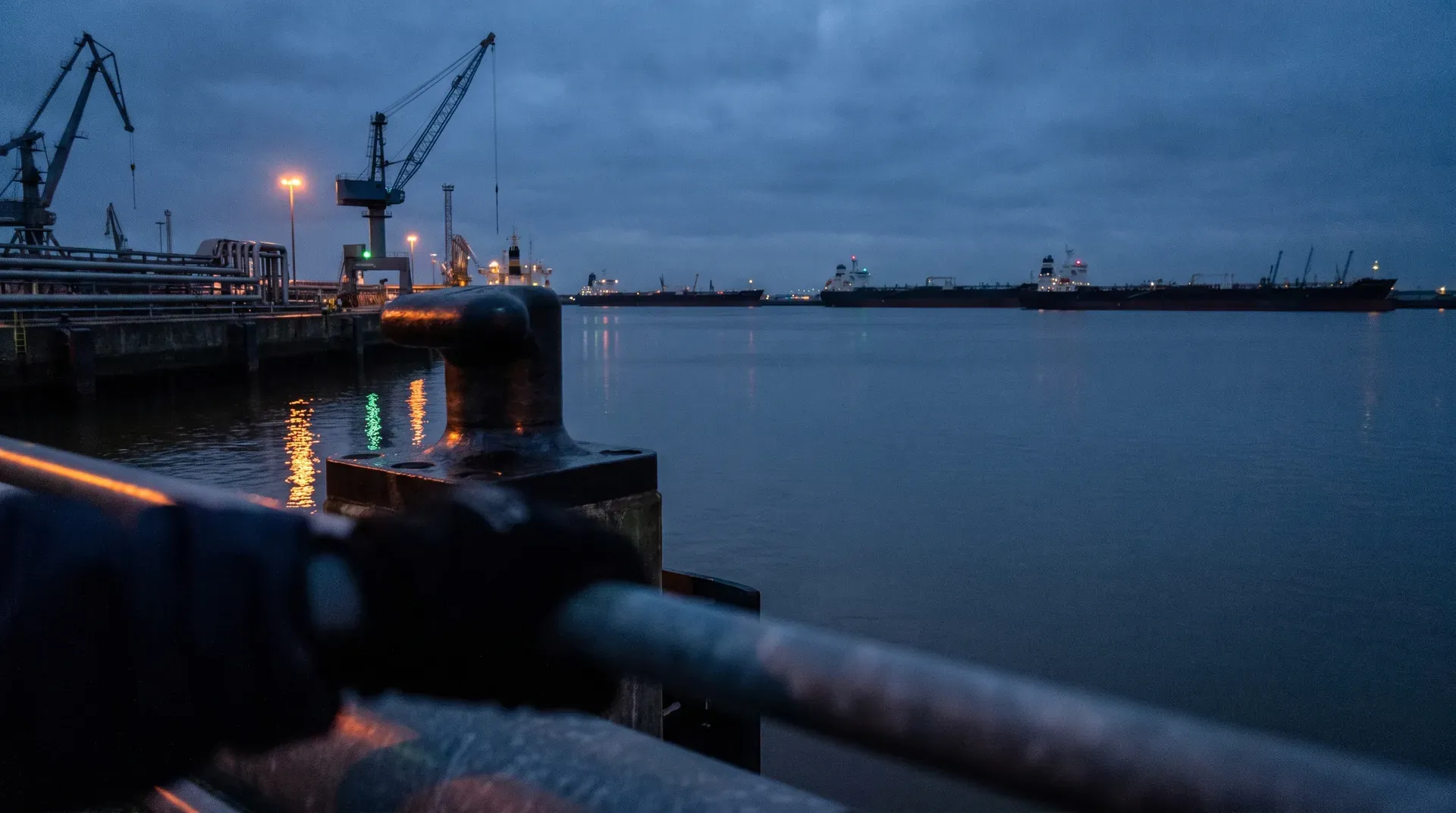 Havenscène bij schemering met tankers op anker, verlichte laadkranen en stille waterspiegels