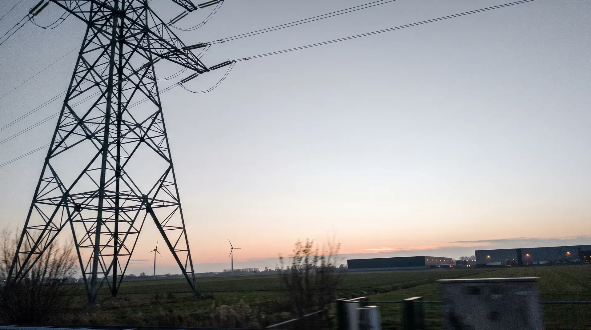 Hoogspanningstoren bij schemering met windmolens en industrie-gebouwen op de achtergrond