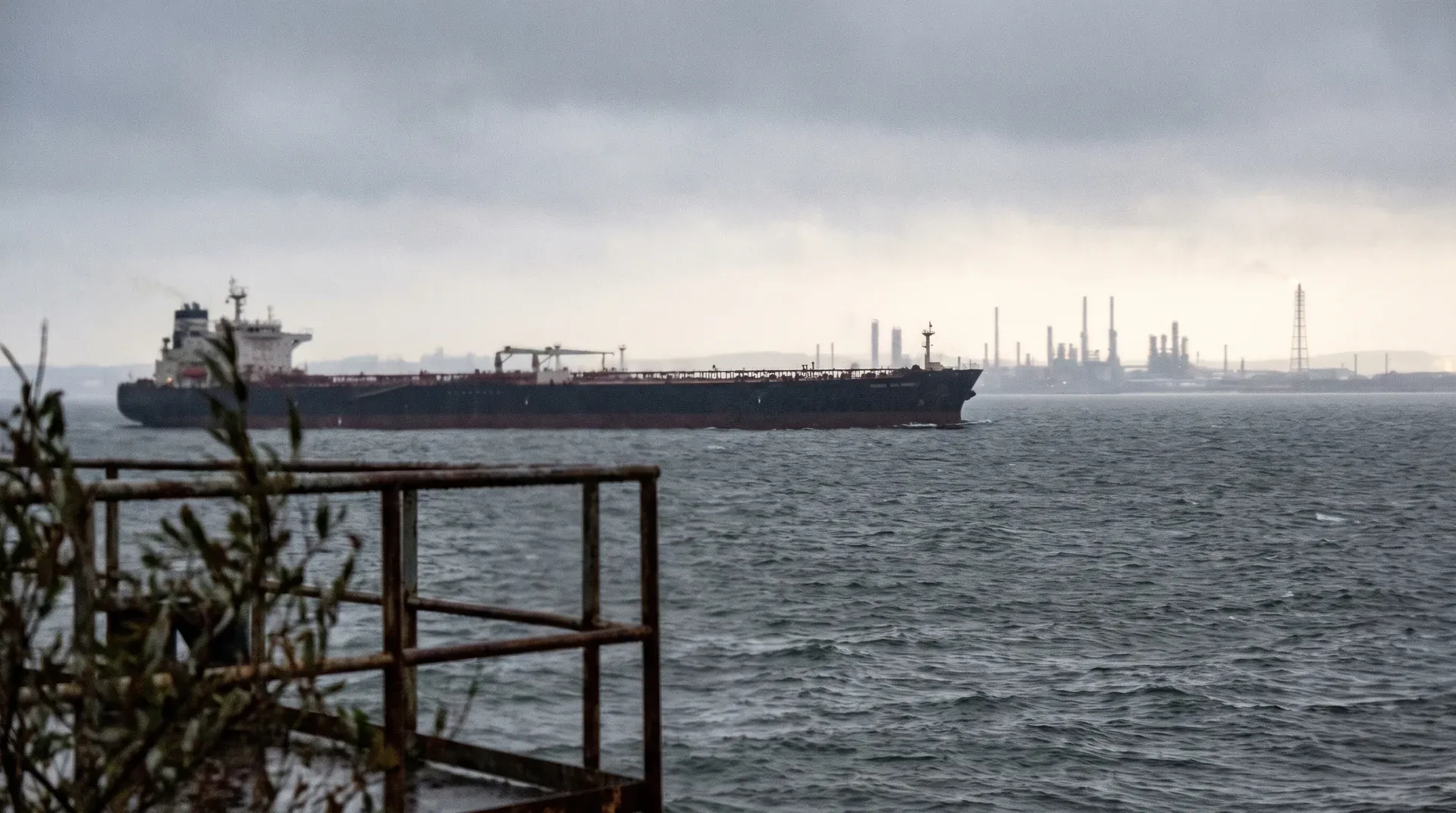 Grote olietanker op zee met industriële raffinaderij en schouwen aan de horizon