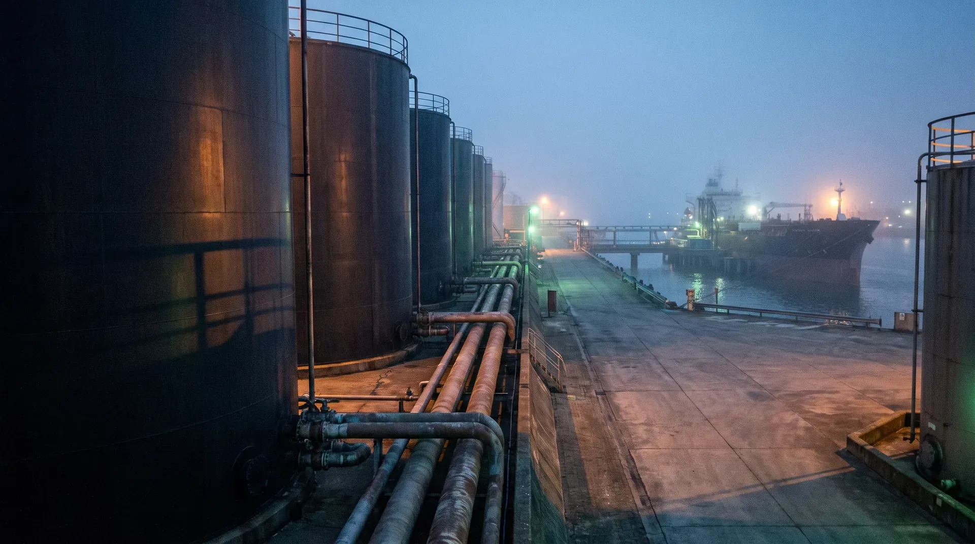 Industriële haveninstallatie met opslagtanks, pijpleidingen en olietanker bij schemering