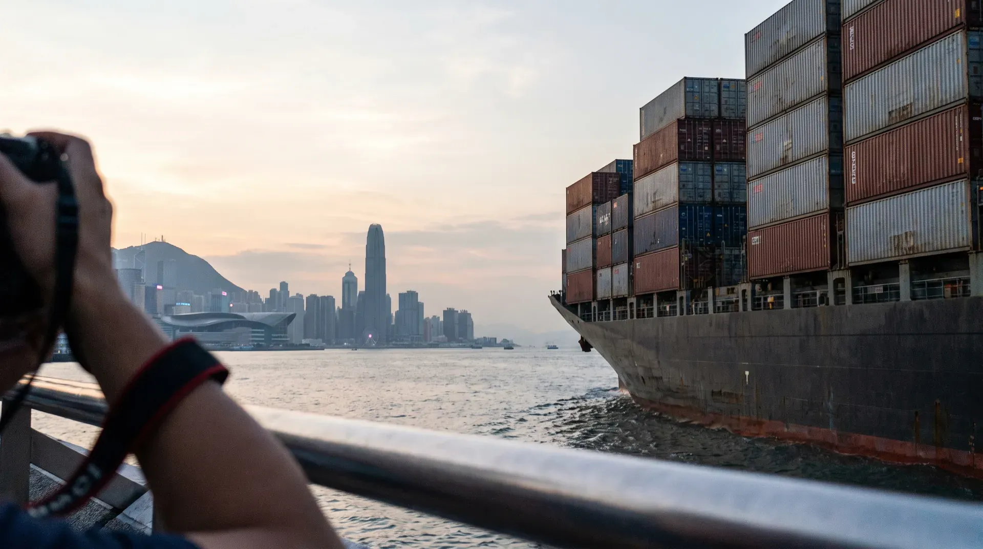 Containerschip met gestapelde lading tegen skyline van Hong Kong bij zonsondergang.