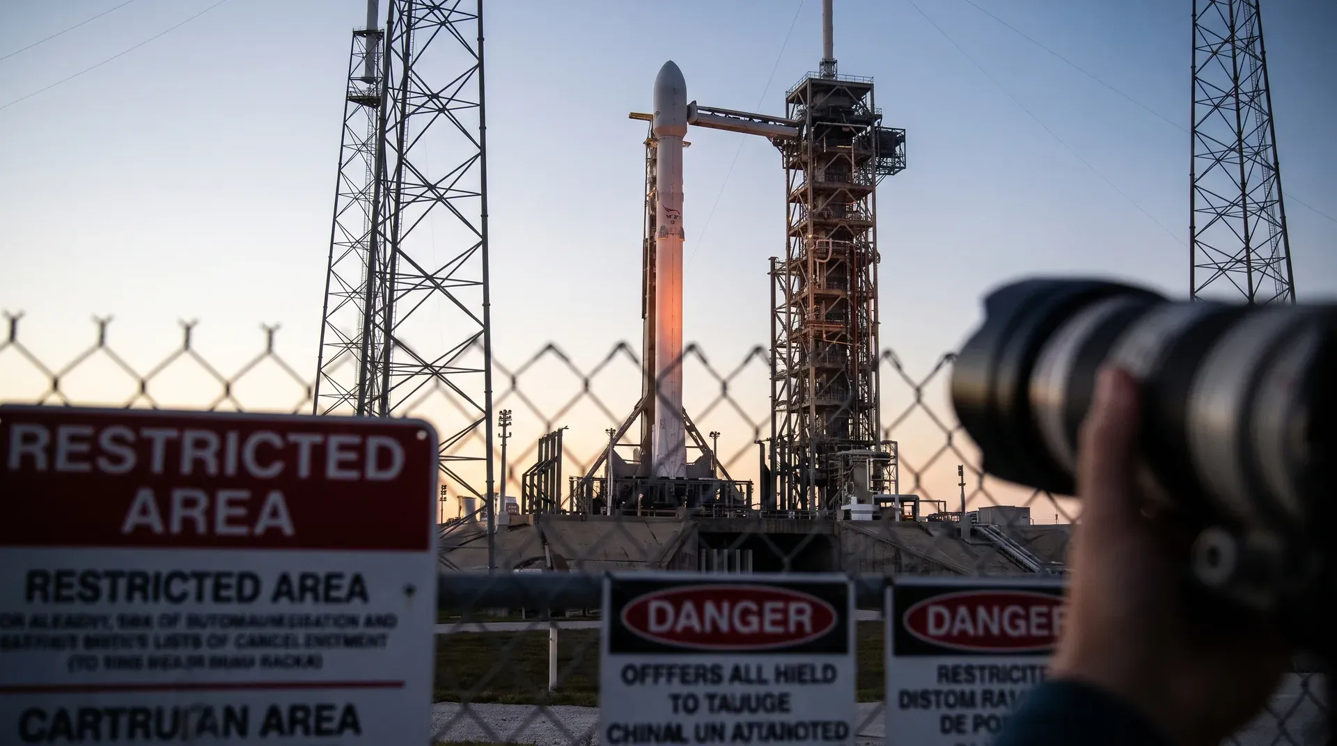SpaceX Falcon 9-raket op lanceerplatform met transporttoren en waarschuwingsborden bij zonsopgang