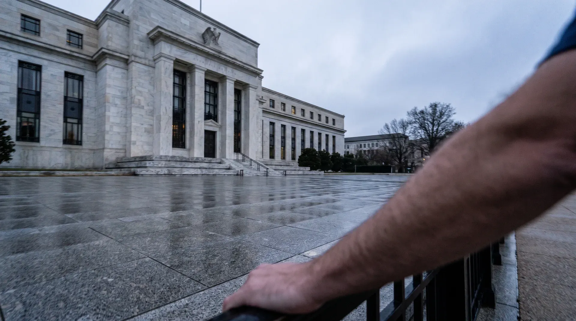 Voorzijde Federal Reserve Building in Washington, met natte plaza en persoon in voorgrond.