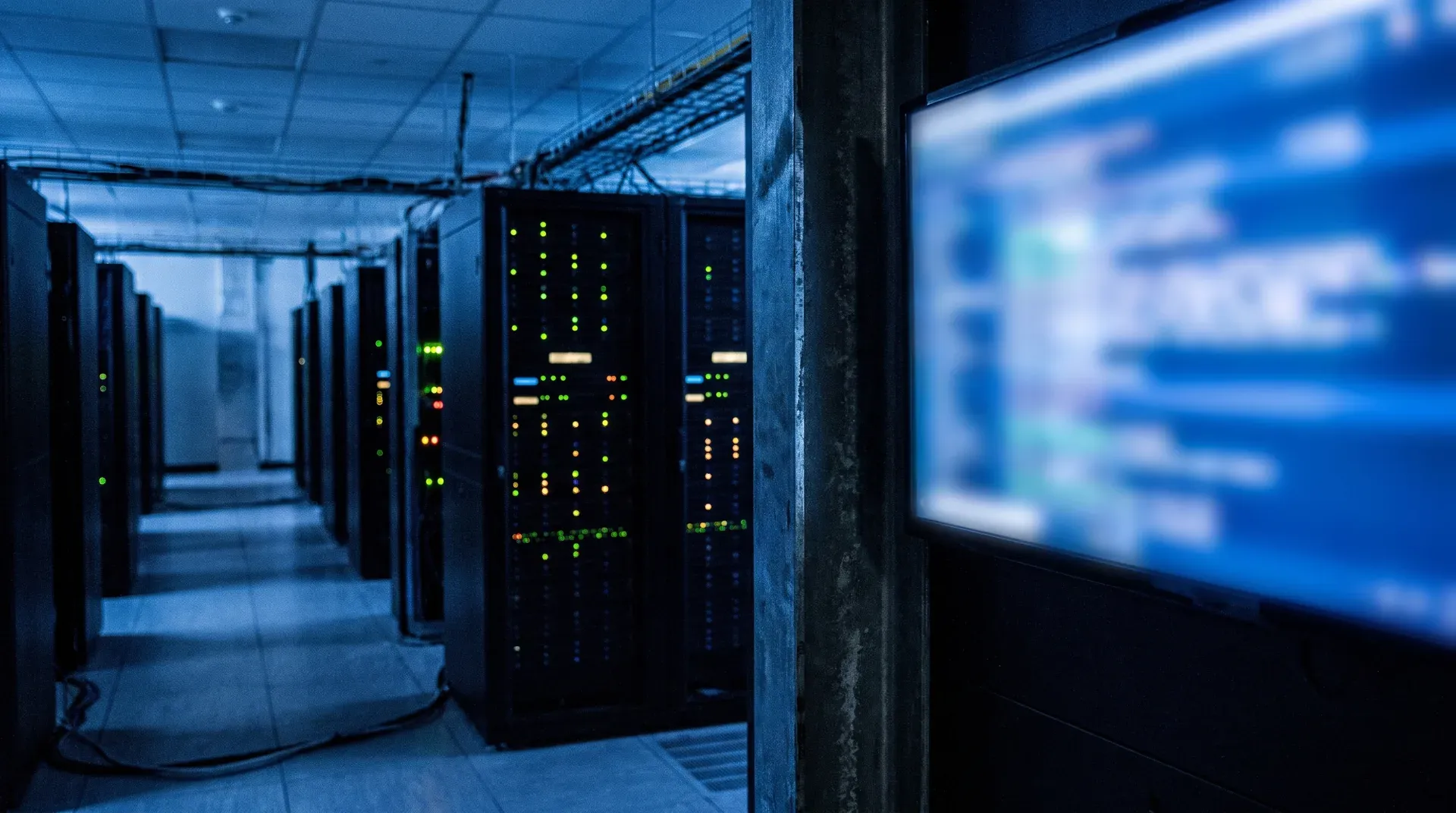 Donkere serverruimte met zwarte kasten en verlichte indicator-leds in blauw licht, monitorscherm rechts
