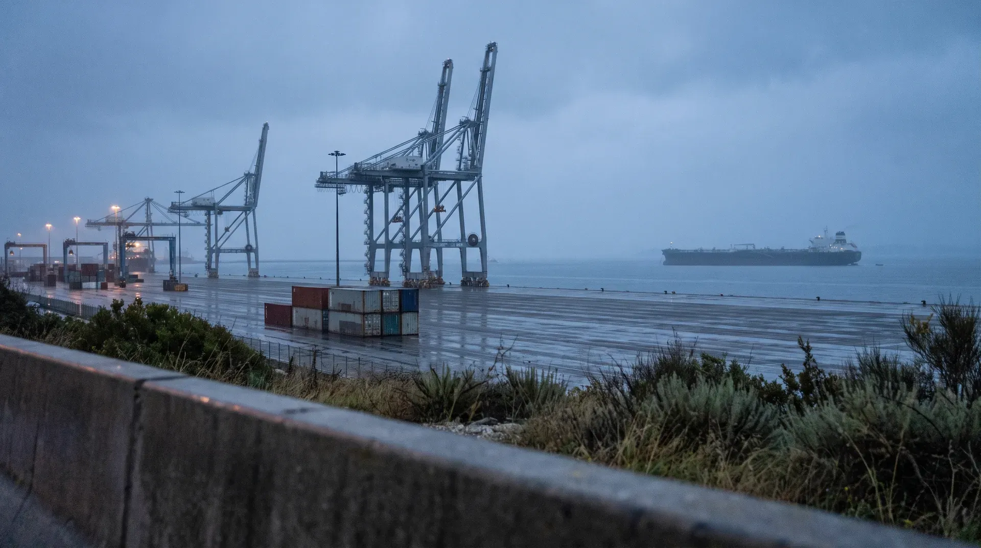 Containerterminal met kraaninstallaties bij schemering, vrachtschip op zee in mist
