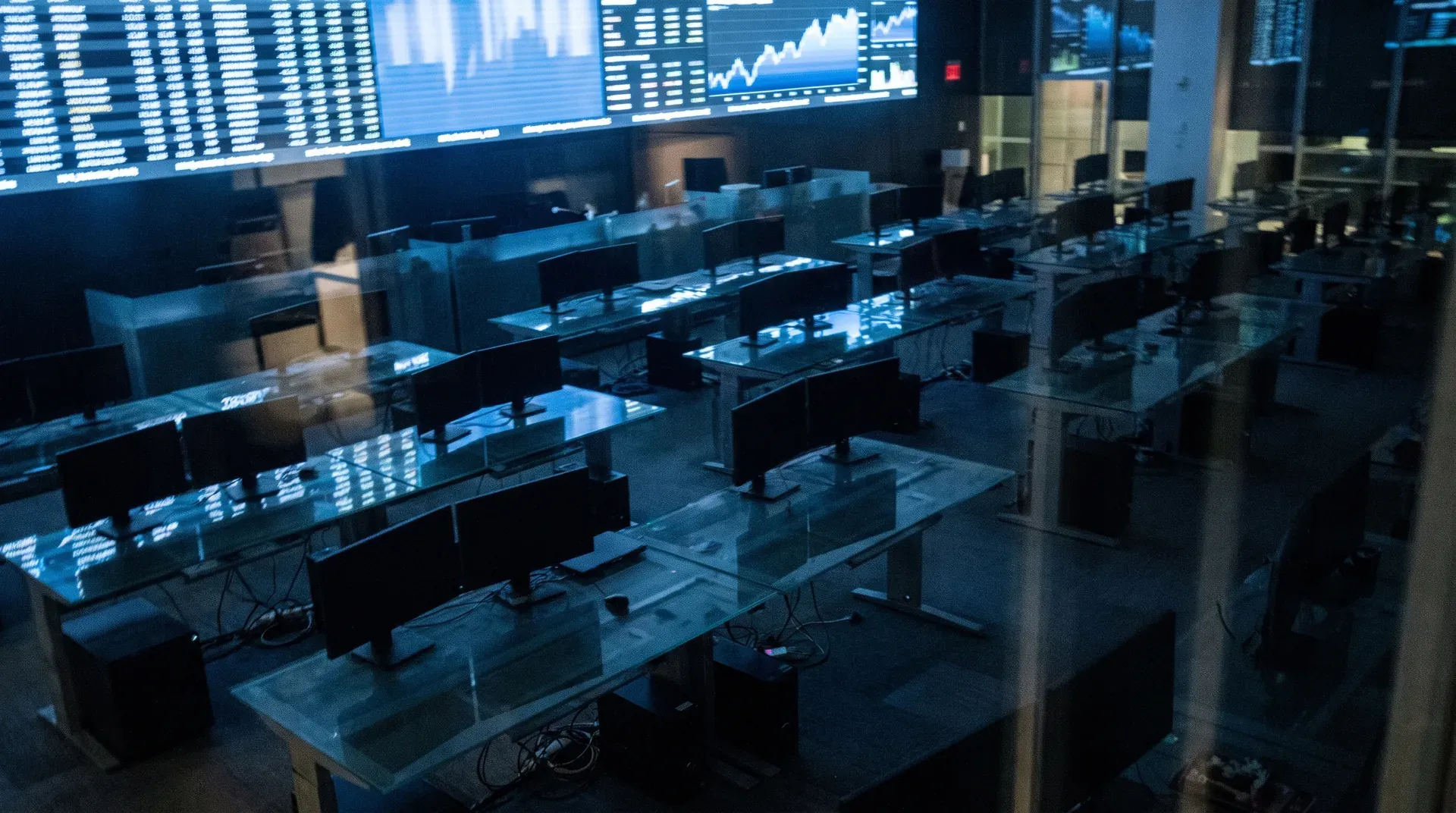 Lege handelsvloer met meerdere monitoren en handelsposten onder grote beursschermen met grafieken
