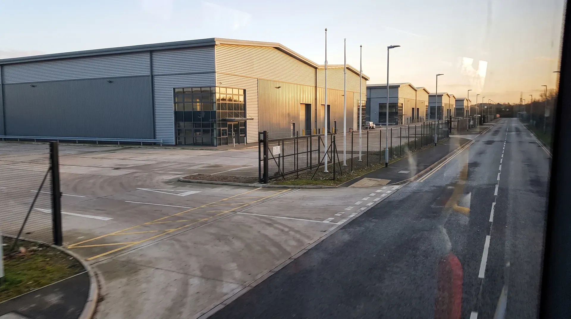 Moderne industriële bedrijfsgebouwen met gele golfplaat langs verlichte weg bij zonsondergang