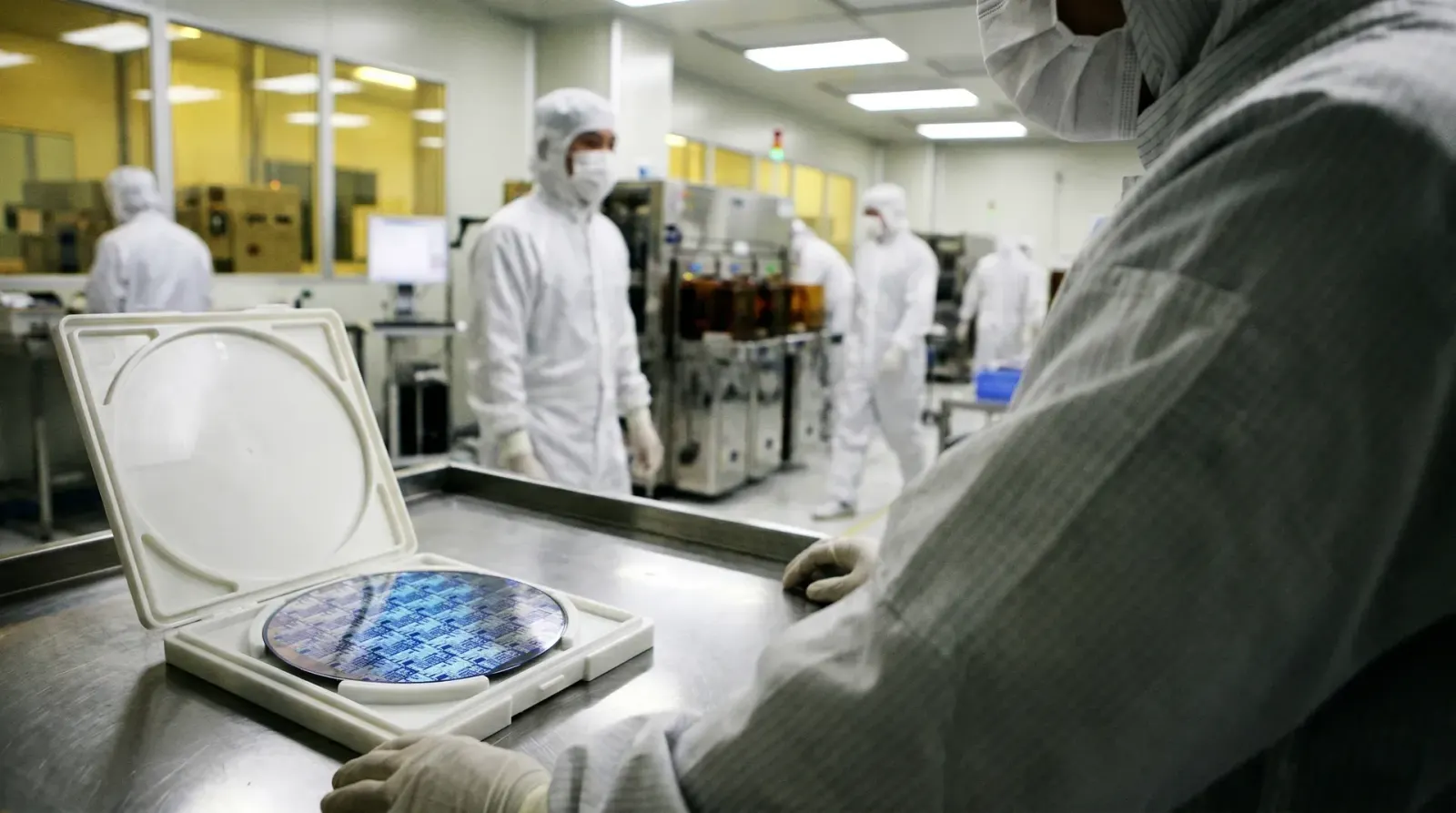Cleanroom-omgeving met werknemers in witte beschermende kleding rond halfgeleiderwafels en verwerkingsapparatuur