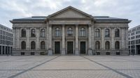 Klassiek stenen overheidsgebouw met zuilen en gevel, symmetrisch gecentreerd op groot plein.