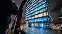 Modern glazen kantoorgebouw 's nachts verlicht met blauwe lichten, persoon op voorgrond