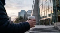 Persoon in donkere jas op groot modern plein voor glazen kantoorgebouwen bij schemering.