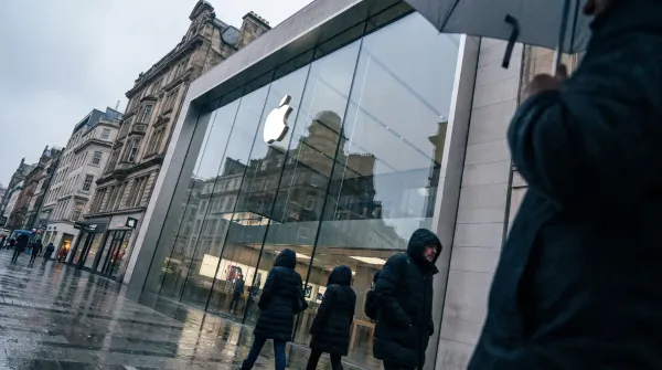 Apple Store met glazen gevel en logo, voetgangers op regennatte straat, historische gebouwen op achtergrond
