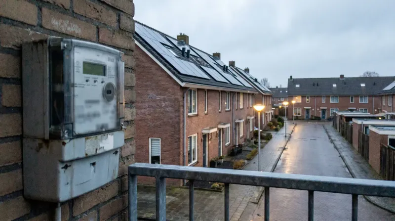 Rij moderne huizen met zonnepanelen op daken, digitale energiemeter op muur, avondschemering.