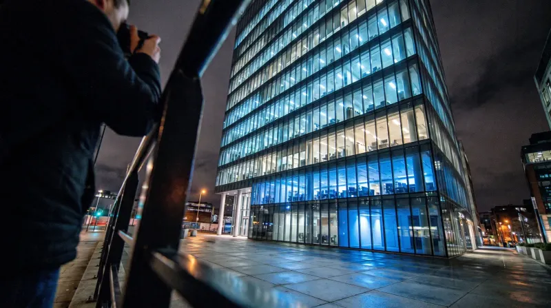 Modern glazen kantoorgebouw 's nachts verlicht met blauwe lichten, persoon op voorgrond