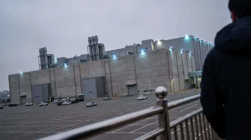 Groot industrieel gebouw met blauwe nachtverlichting, parkeerterrein met auto's, schemering