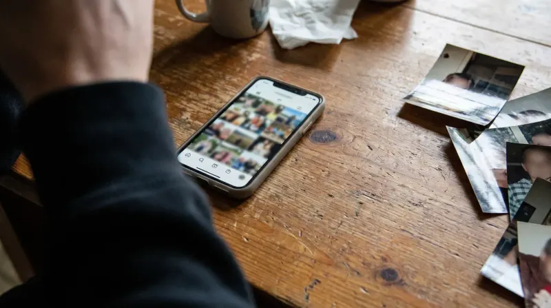 Persoon bekijkt smartphone met Instagram-feed op houten tafel naast uitgeprinte foto's