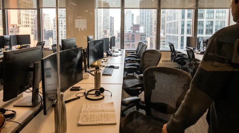 Modern kantoorruimte met bureaus, computermonitoren en ergonomische stoelen met skyline-uitzicht.