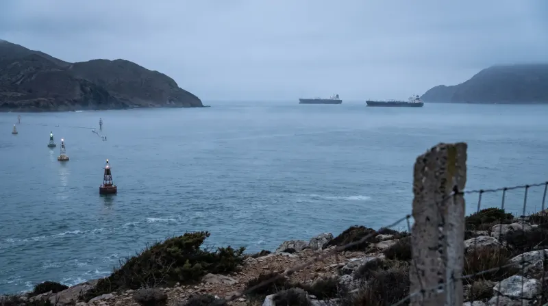 Ankergebied met vrachtschepen in baai omgeven door rotsachtige kustlijn en bergen