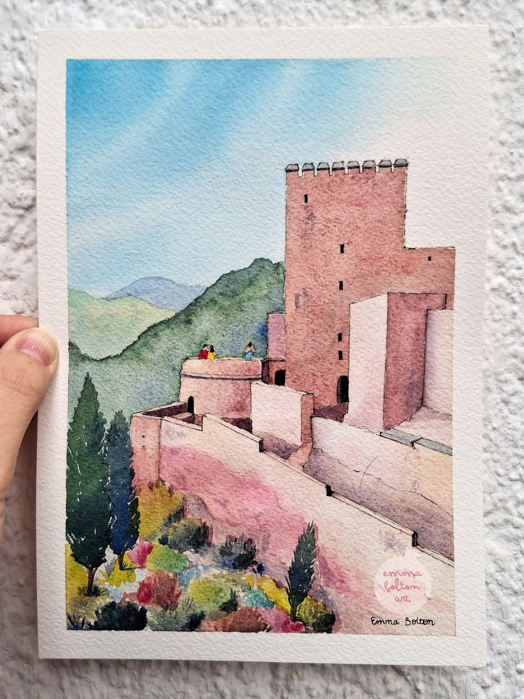 Watercolour painting by Emma Bolton of La Alcazaba at the Alhambra, Granada. It's a pink castle with complicated levels surrounded by mountains and a beautiful garden. 