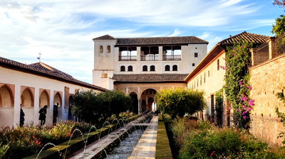 The Court of the River at the Generalife in Granada. In front of the two-storey white palace are gardens, a long fountain and archways.
