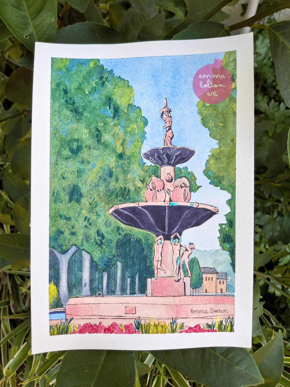 A watercolour painting of the pomegranate fountain in central Granada by Emma Bolton on a background of leaves.