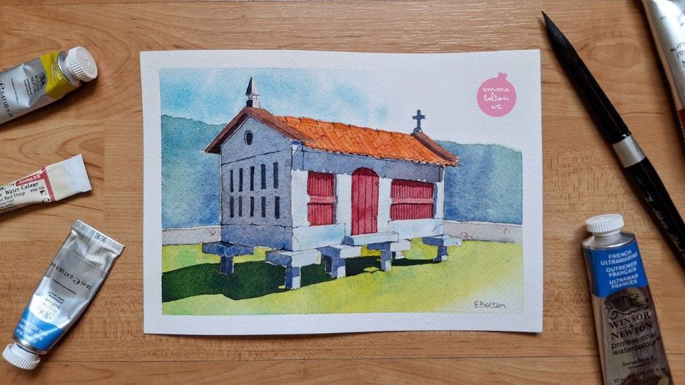 Watercolour painting of a grey, stone hórreo with a red wooden door and orange, tiled roof. It sits on green grass with mountain in the distance. 