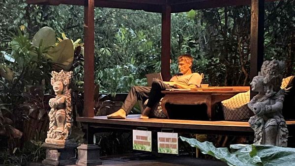 Digitaler Nomade am Pool in Ubud mit Laptop bei Regen – ortsunabhängiges Einkommen als Basis für Auswanderung mit Familie
