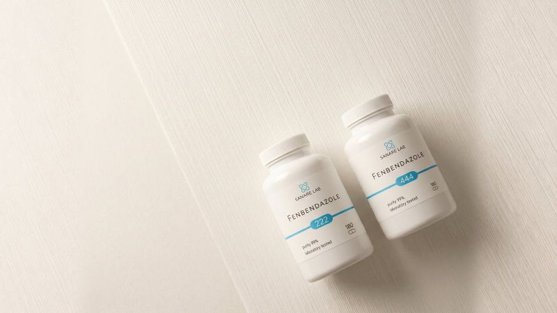 Two Sanare Lab Fenbendazole bottles, 222 mg and 444 mg, on a light wooden surface