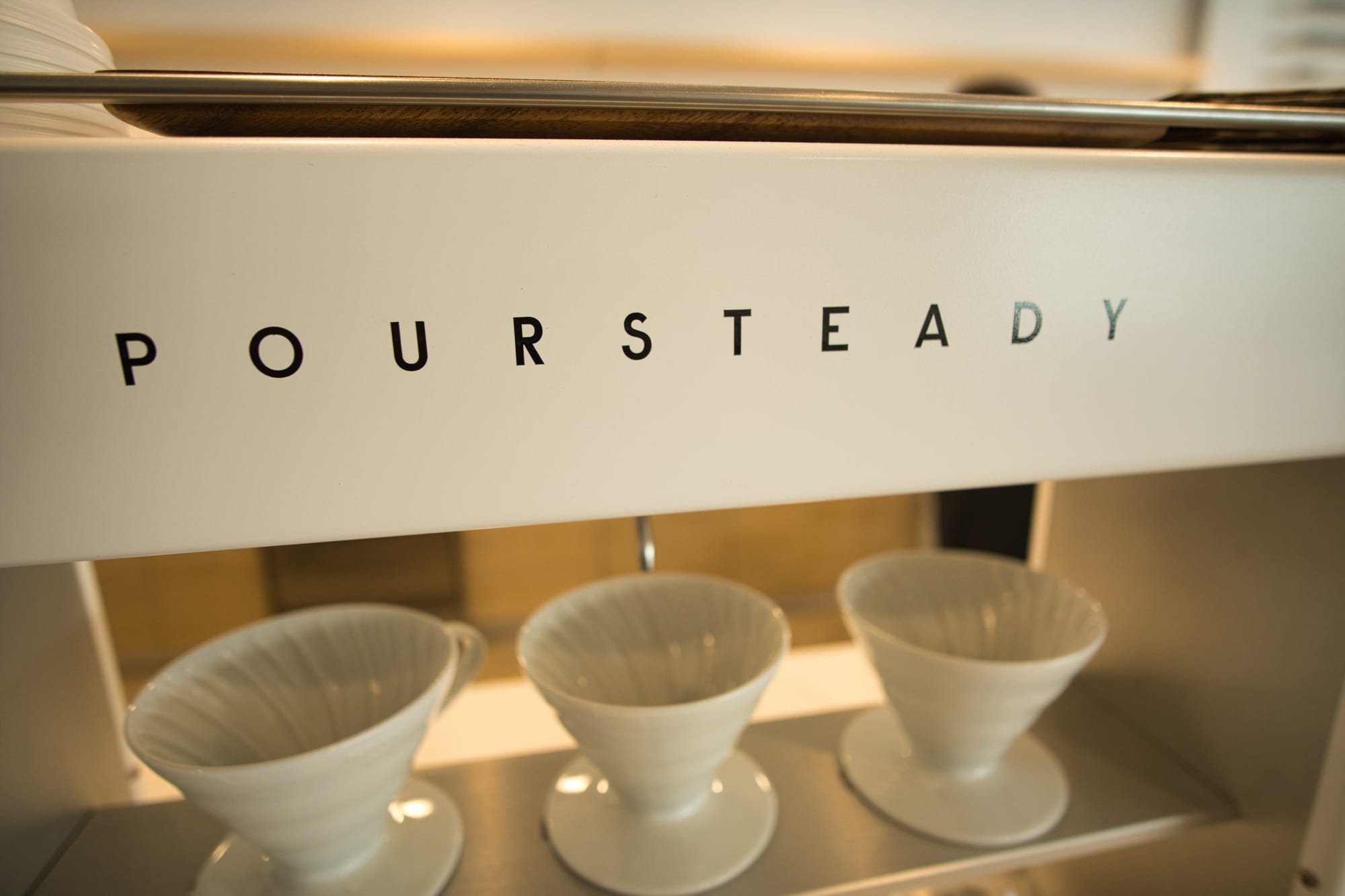 Poursteady coffee machine at For Keeps Coffee House with white glass coffee mugs sitting on the shelf underneath the pour spouts