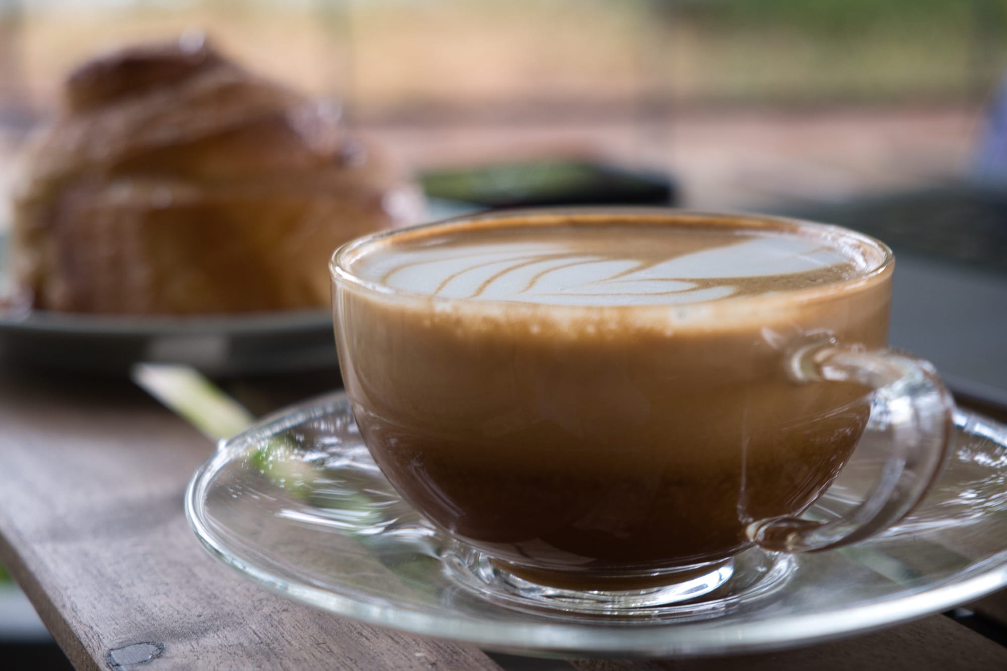A glass with a latte and a cinnamon roll in the backdrop at Street Dog Cafe in Waco, Tx