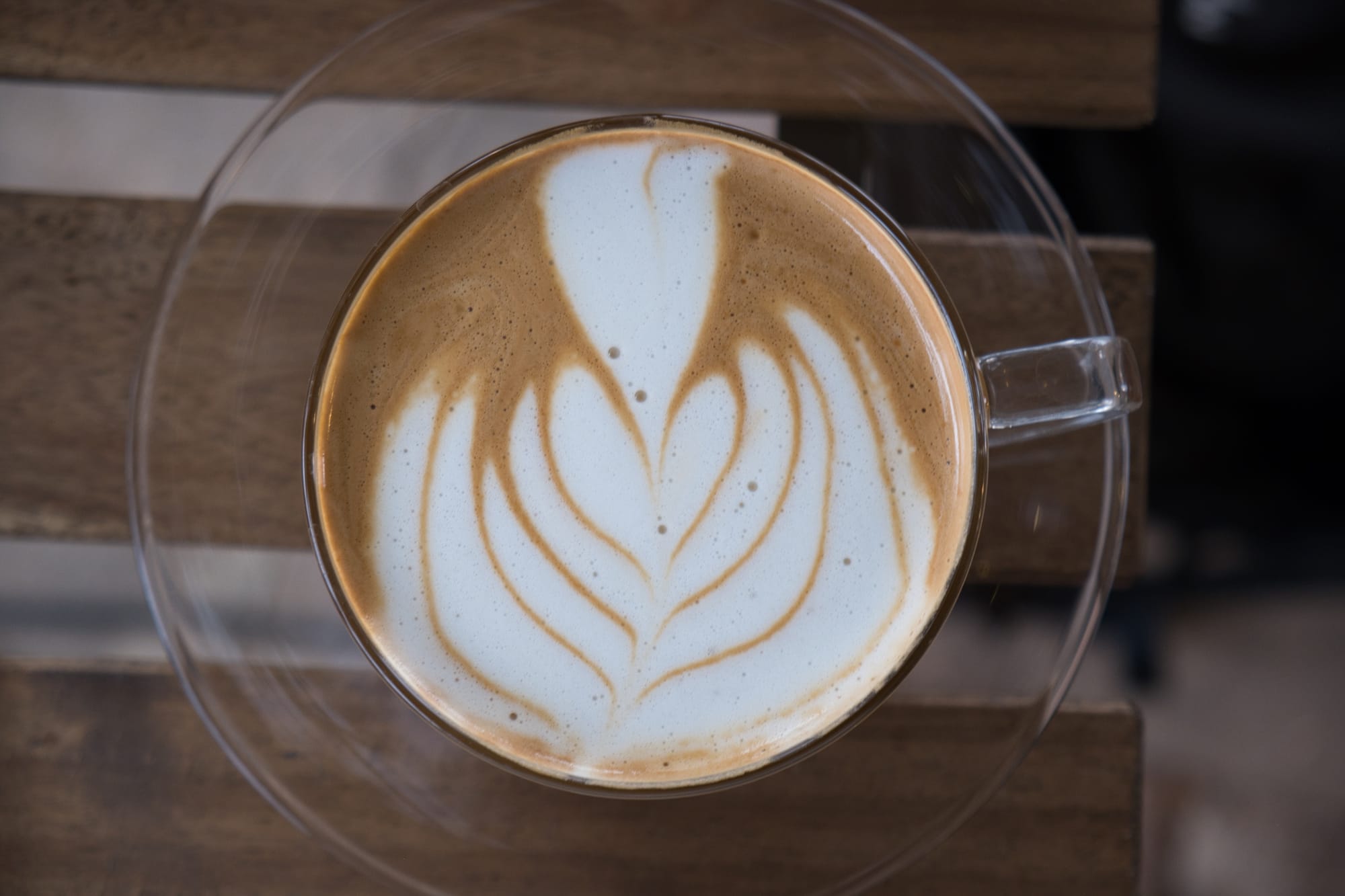 A latte with a flower art on top in a clear white glass on a glass plate at Street Dog Cafe in Waco Texas