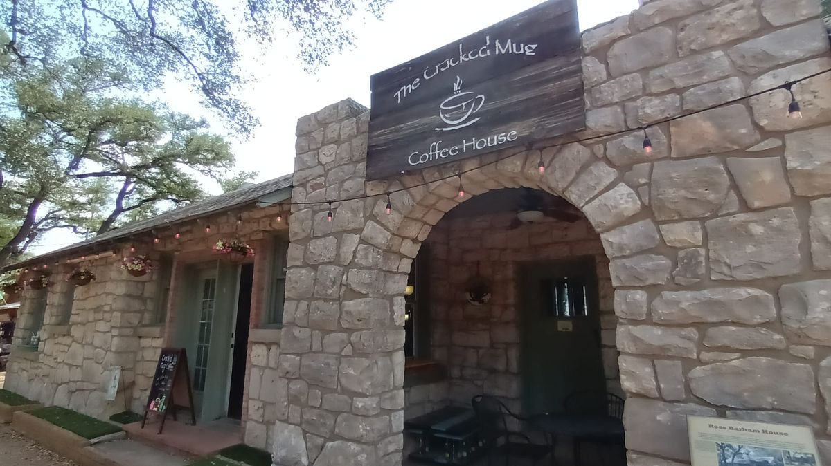 the front of The Cracked Mug Coffee House entrance in a building made of stone in old-town Helotes