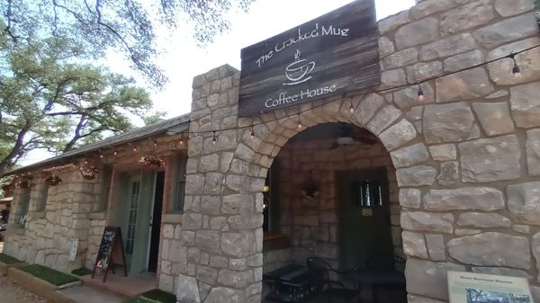 the front of The Cracked Mug Coffee House entrance in a building made of stone in old-town Helotes