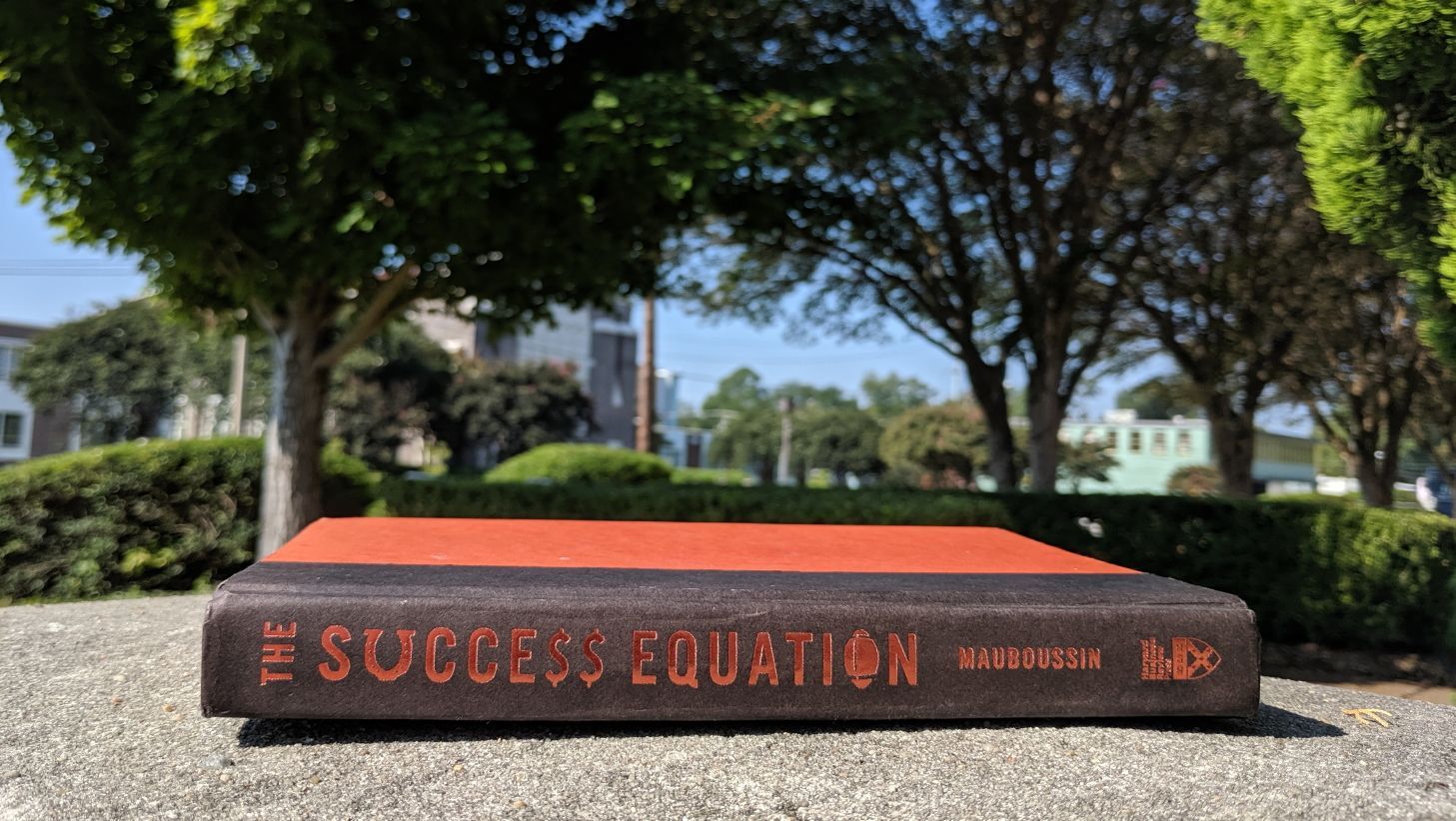 Side profile of The Success Equation by Michael Mauboussin on a concrete surface with trees in the background.