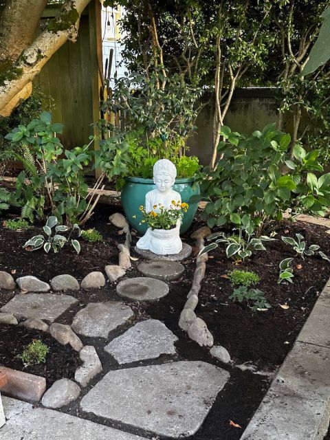 Welcoming statue of Kuan Yin with flowers in front garden, by David Bilides