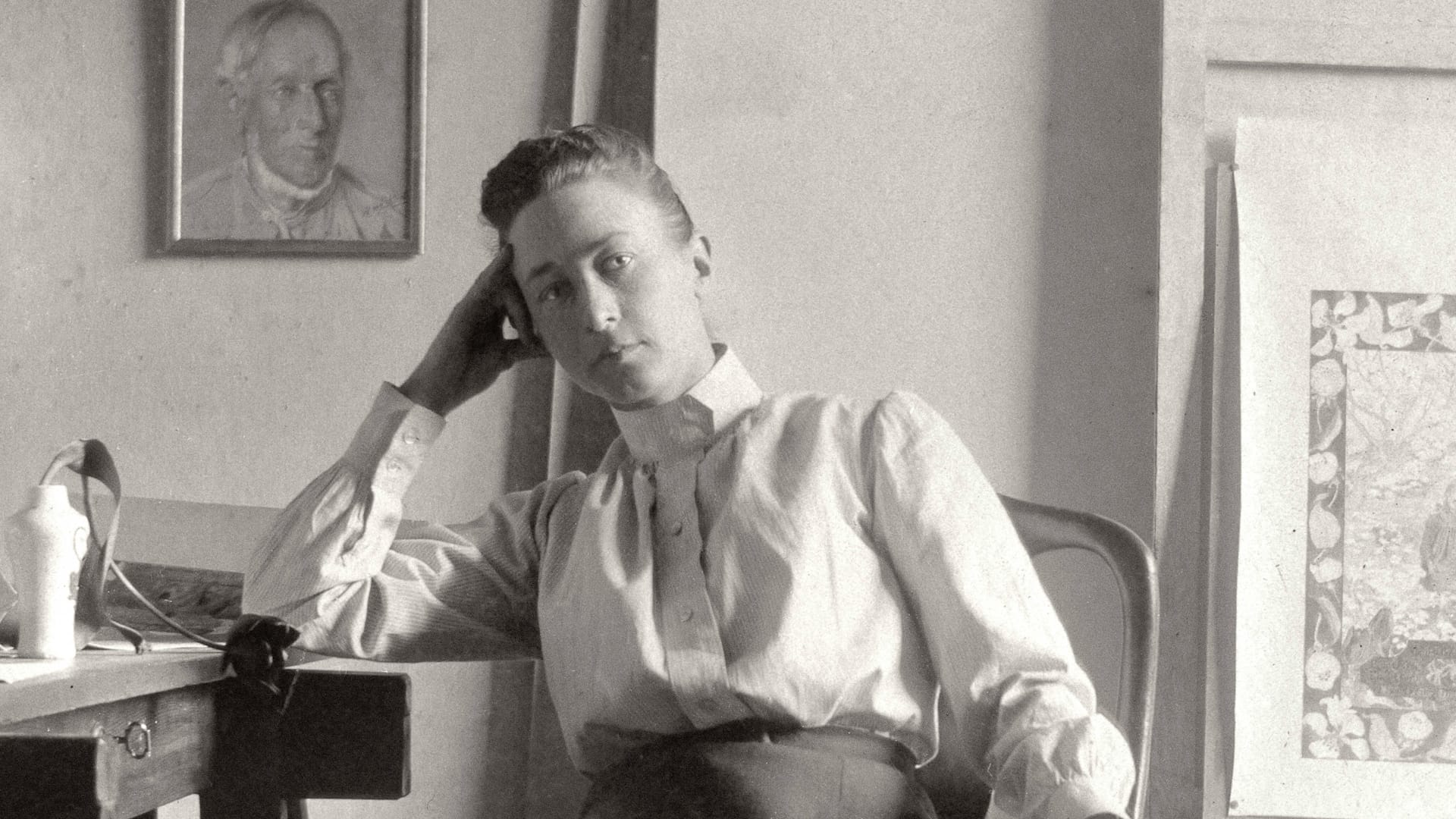 Photo of Hilma af Klint, sitting in a chair facing the camera, her right arm on a desk holding her head up.