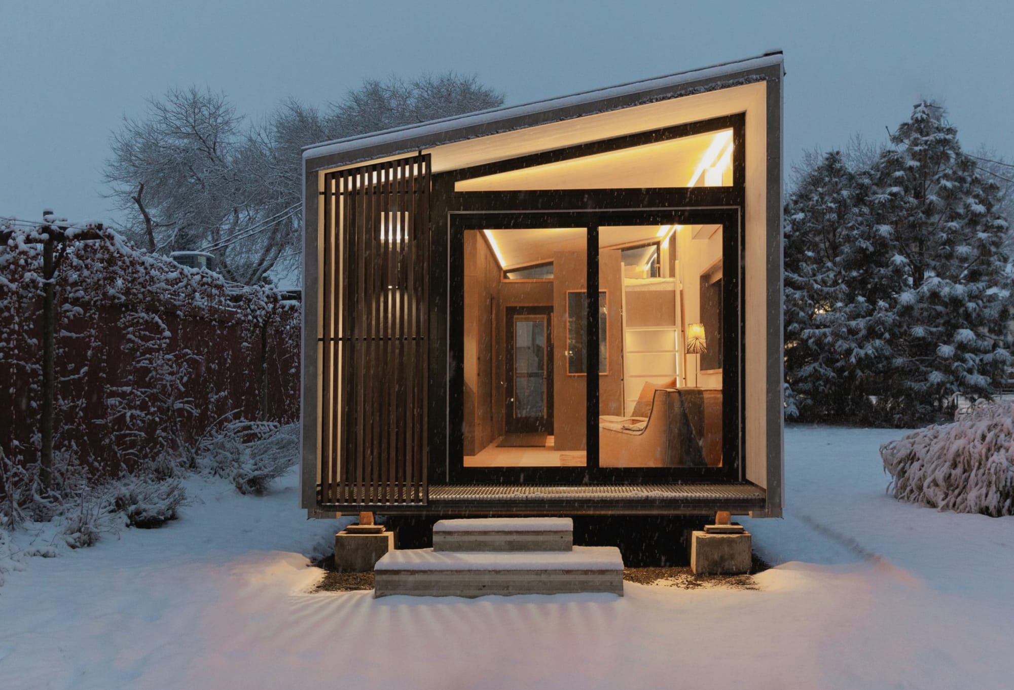 Photo of a small cabin lit internally on a winter evening.