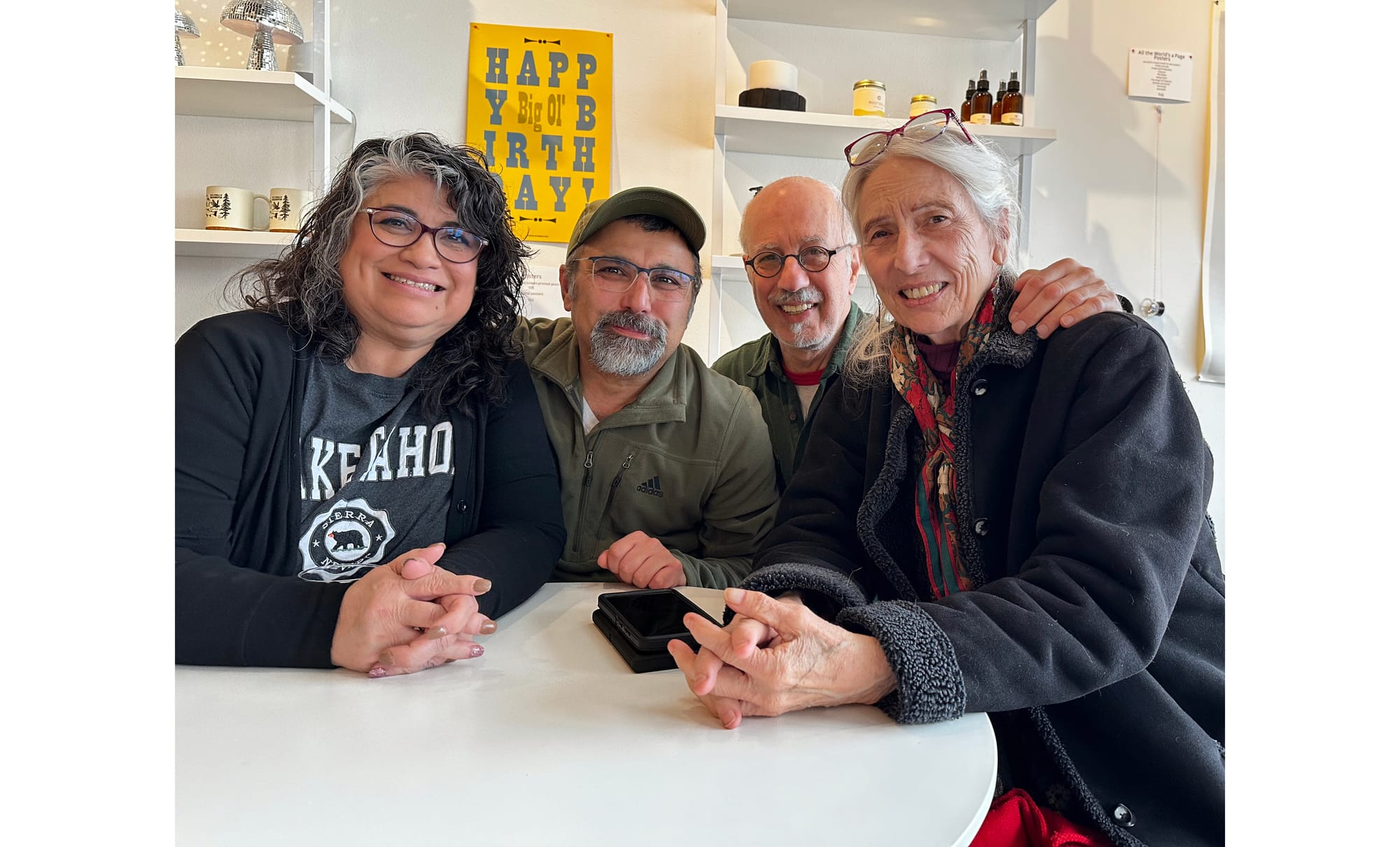 Two upbeat couples sitting at a small table inside a cafe.