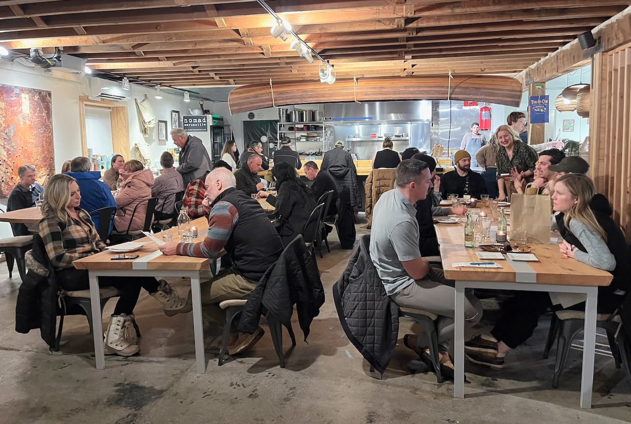 Three long tables of diners in front, with a hanging canoe over the cooks' counter at the back of a large room.