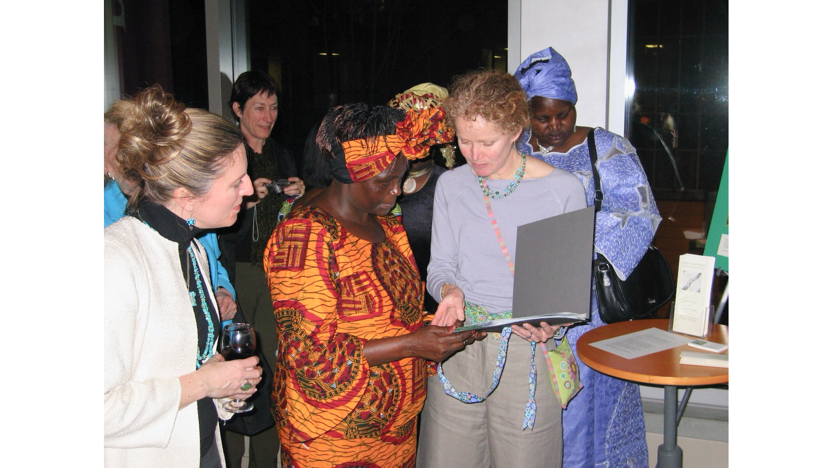 Photo of African woman and American artist looking at a notebook, with other women around them