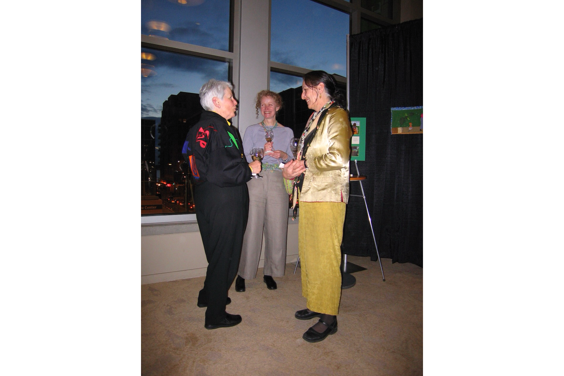 Photo of 3 women holding drinks and chatting in front of window
