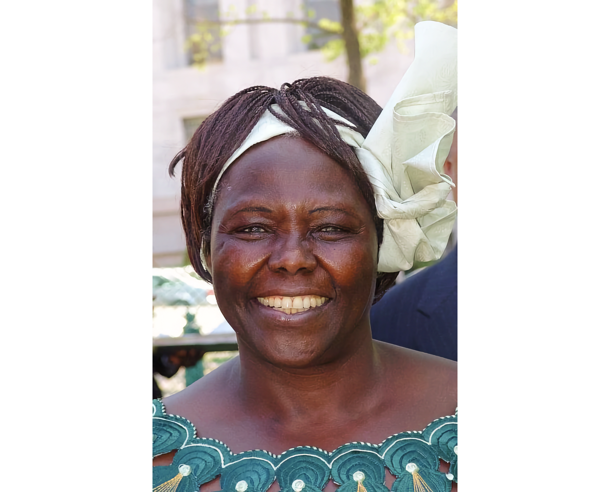 Portrait photo of Wangari Maathai, smiling, wearing white headband, showing top of blue print dress.