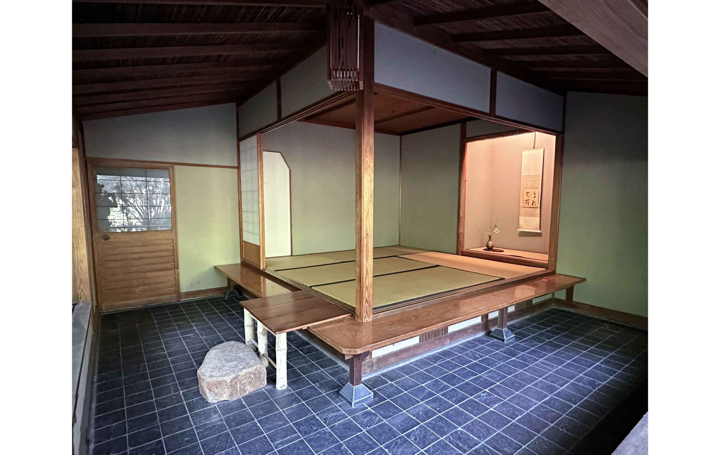 Photo of room with blue tile and light green walls, raised covered wooden platform and wall inset on right with scroll and flower in vase