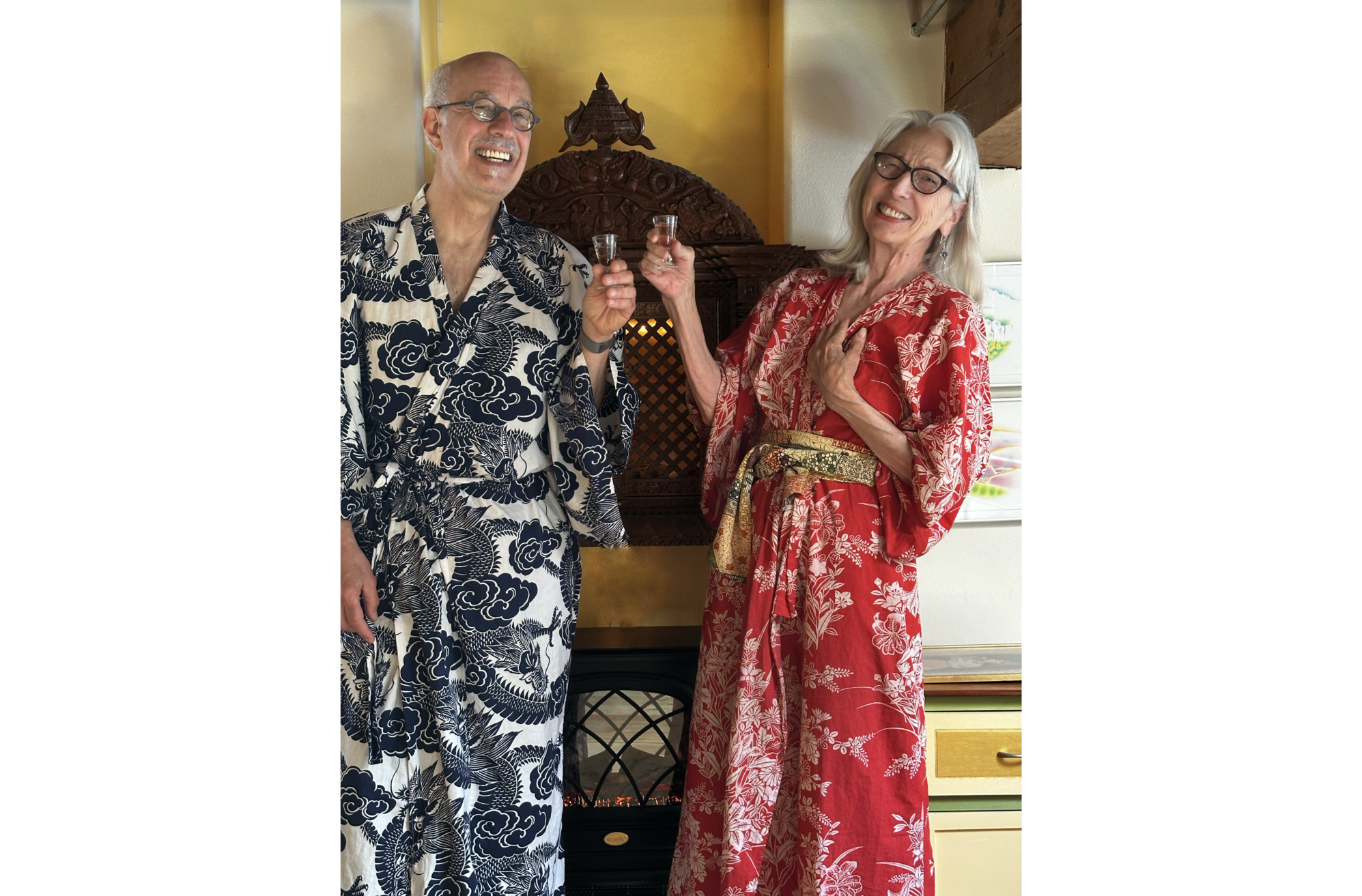 Phot of David in blue and white yukata, and Sandra, in red and white yukata, holding small classes and smiling, in front of Indonesian shrine