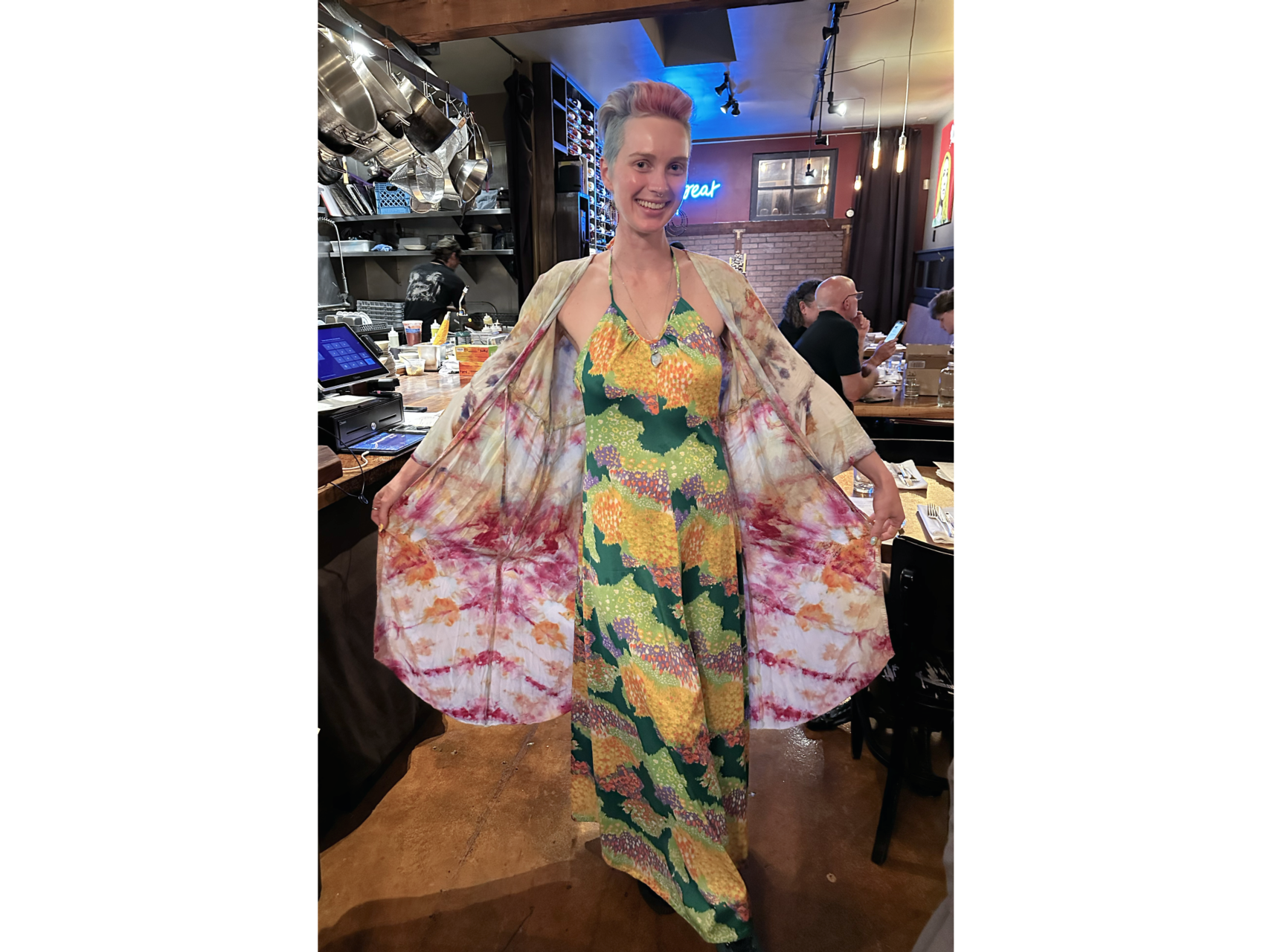 Photo of thin women wearing gree and yellow dress and white and red shawl, facing camera, with tables in background