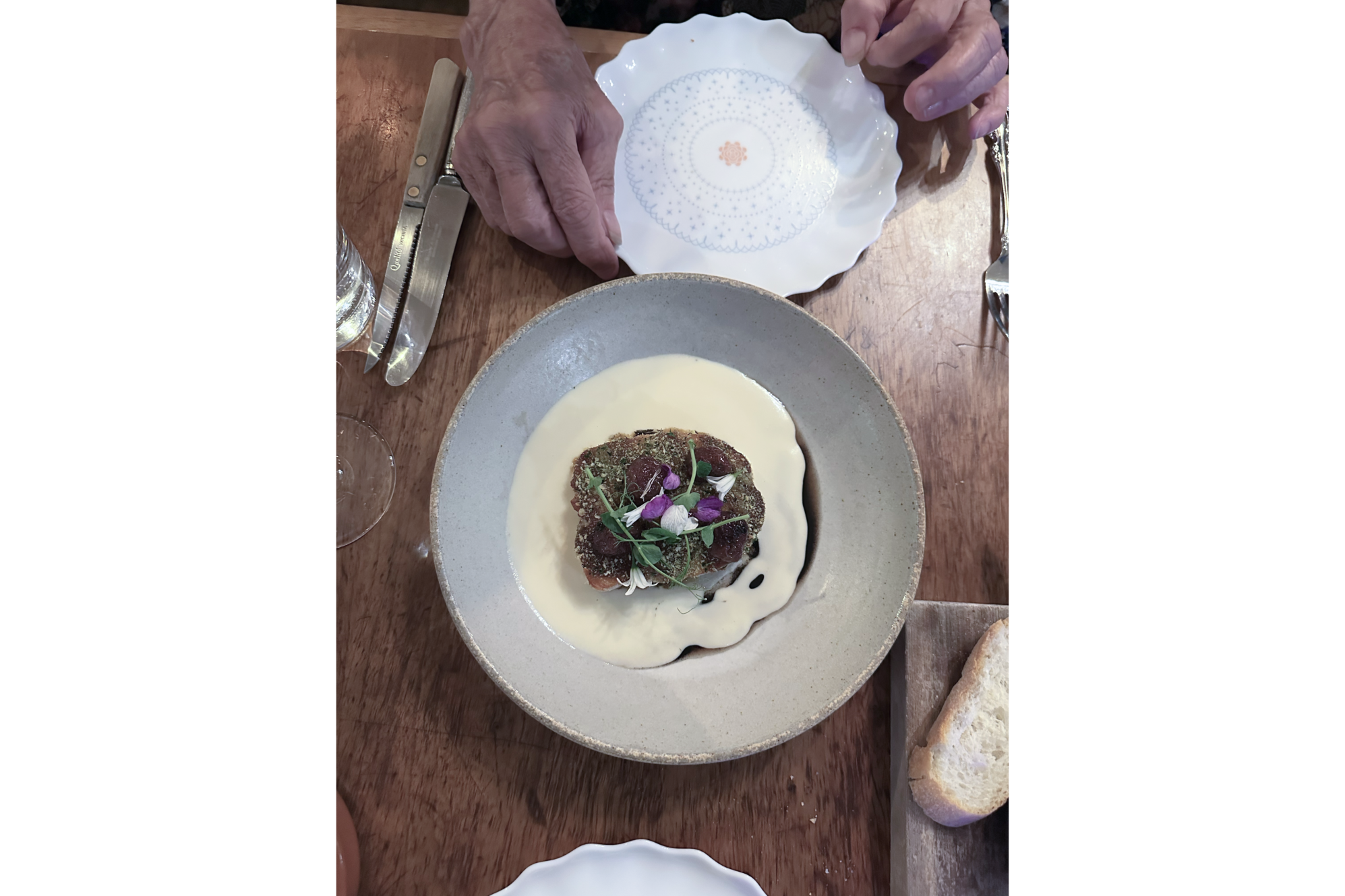 Photo of browned halibut in white sauce and flowers, in shallow grey bowl on dinging table