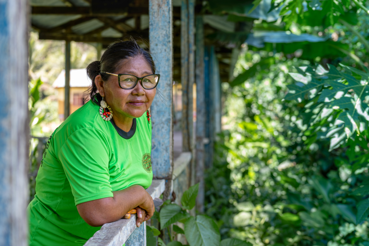 Photo of a Peruvian women in glasses, wearing a green shirt, ornamental earrings, leaning on a railing of a porch