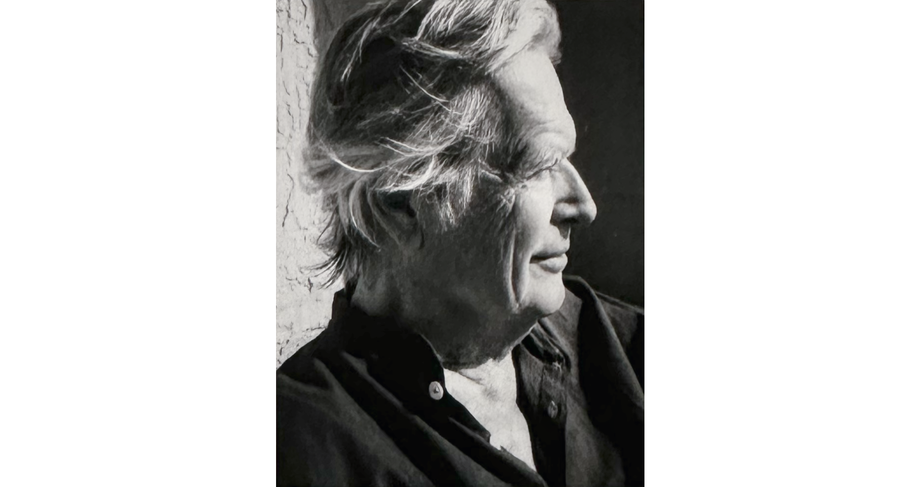 Black and white photo headshot of an elder man with white hair and dark shirt in profile facing to right