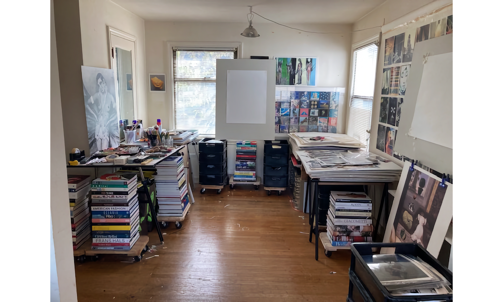 Picture or art studio room with books, drawings, easels, and posters in a white room lit by sunlight.