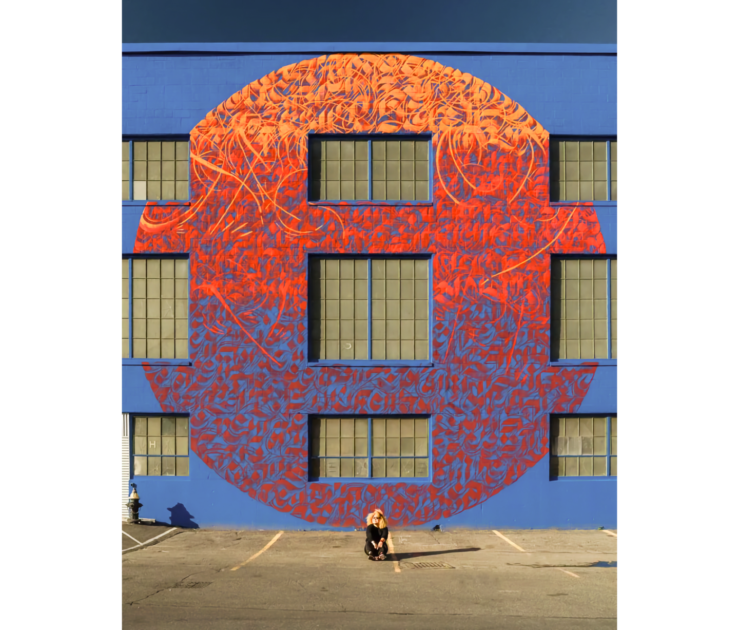 Photo of woman seated in front of 3-story building with large section painted in bright colors in ovoid design